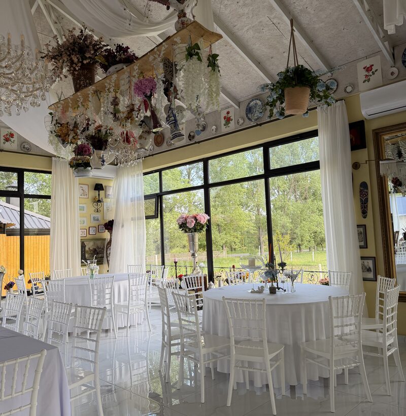 Round tables laid in white beneath dried flowers hung from the beam, the garden through tall windows