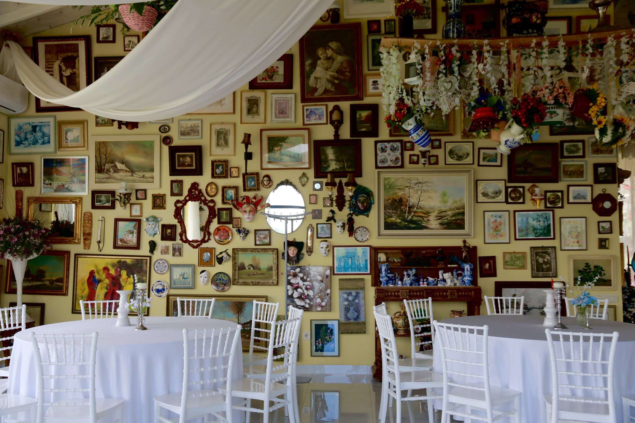 Round tables laid in white beneath the wall of paintings, mirrors and masks