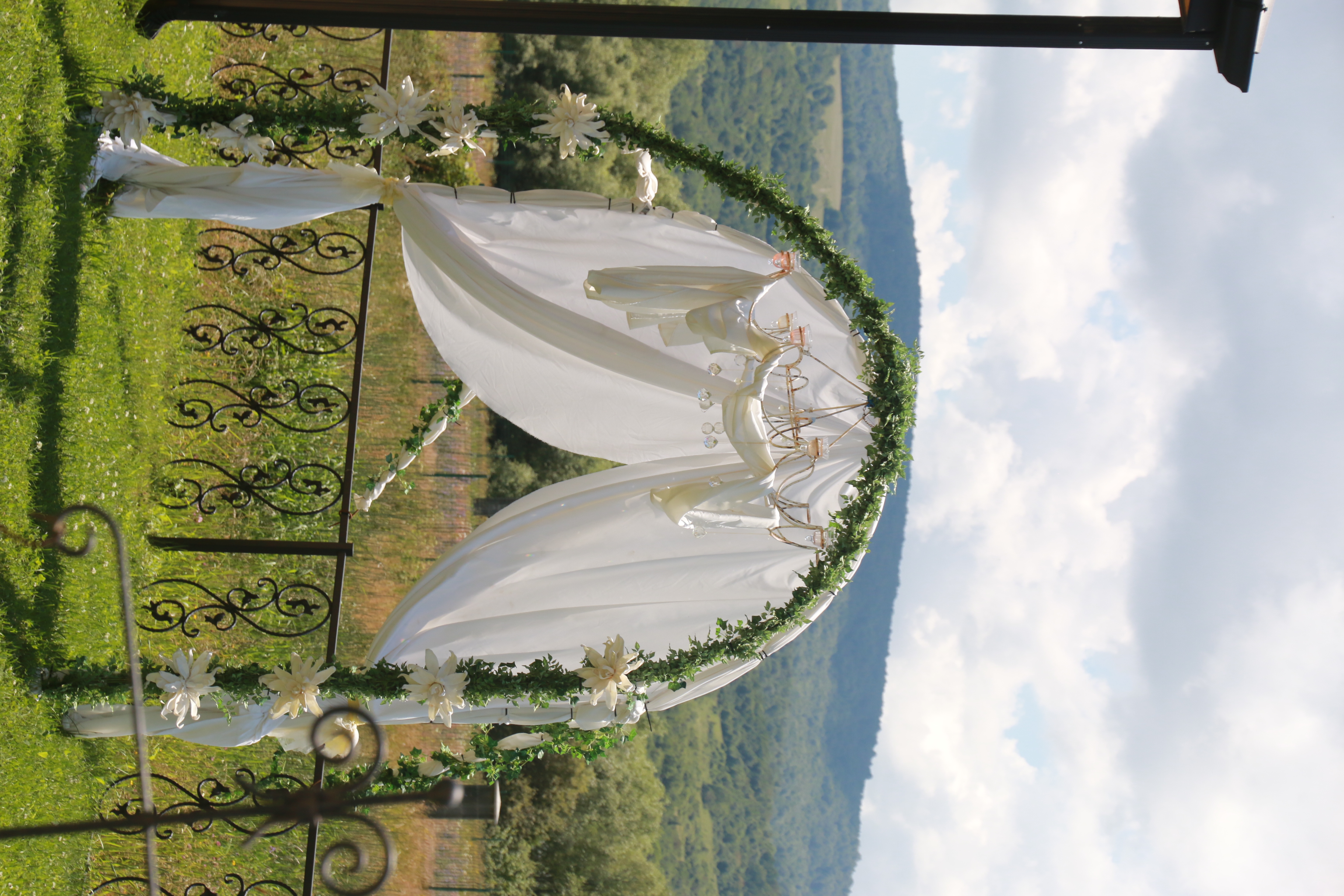 A flower-covered wedding arch on the lawn, with the hills of Tianeti beyond