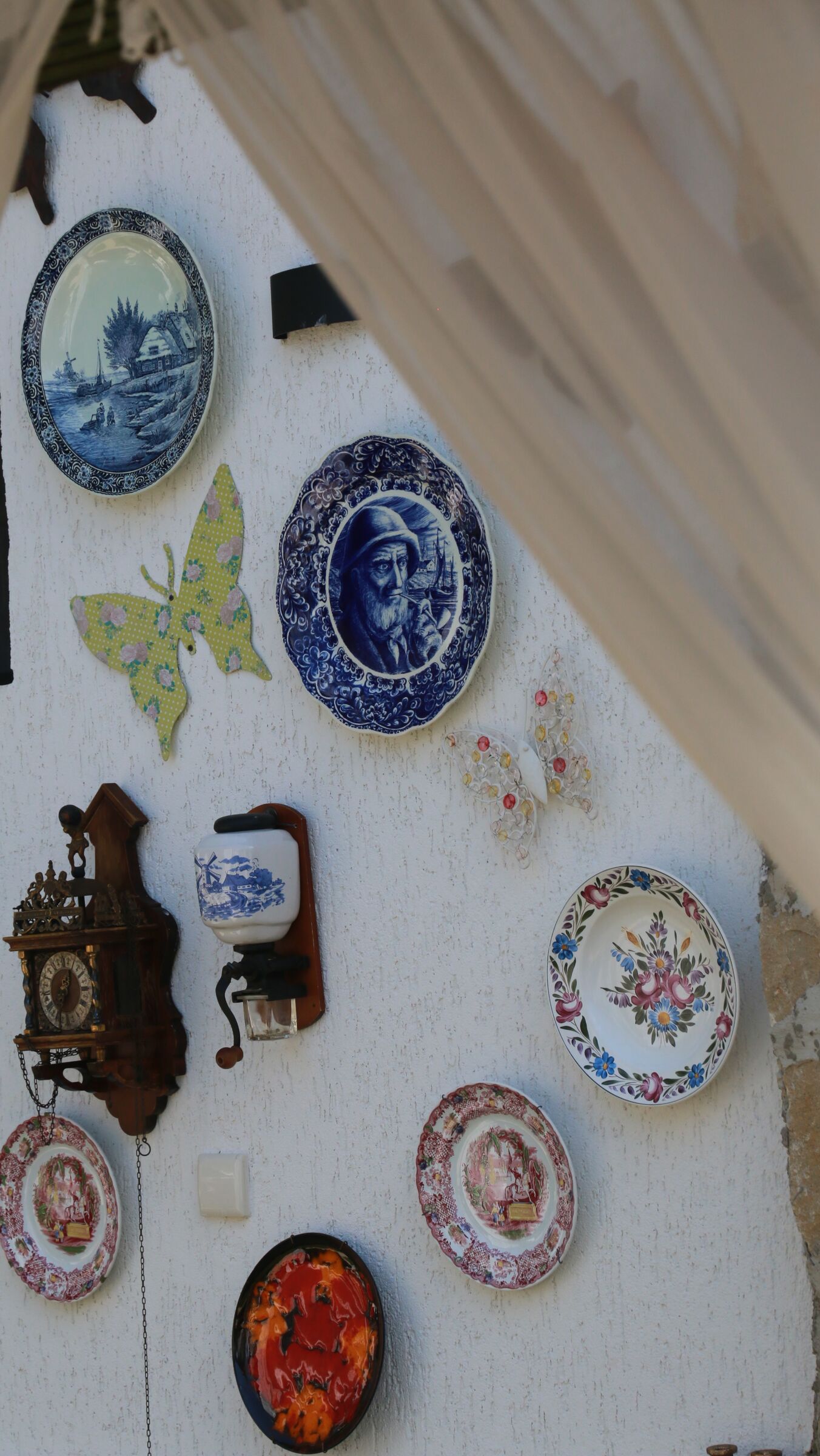 Old painted plates, a butterfly and a wall clock hung on white stucco