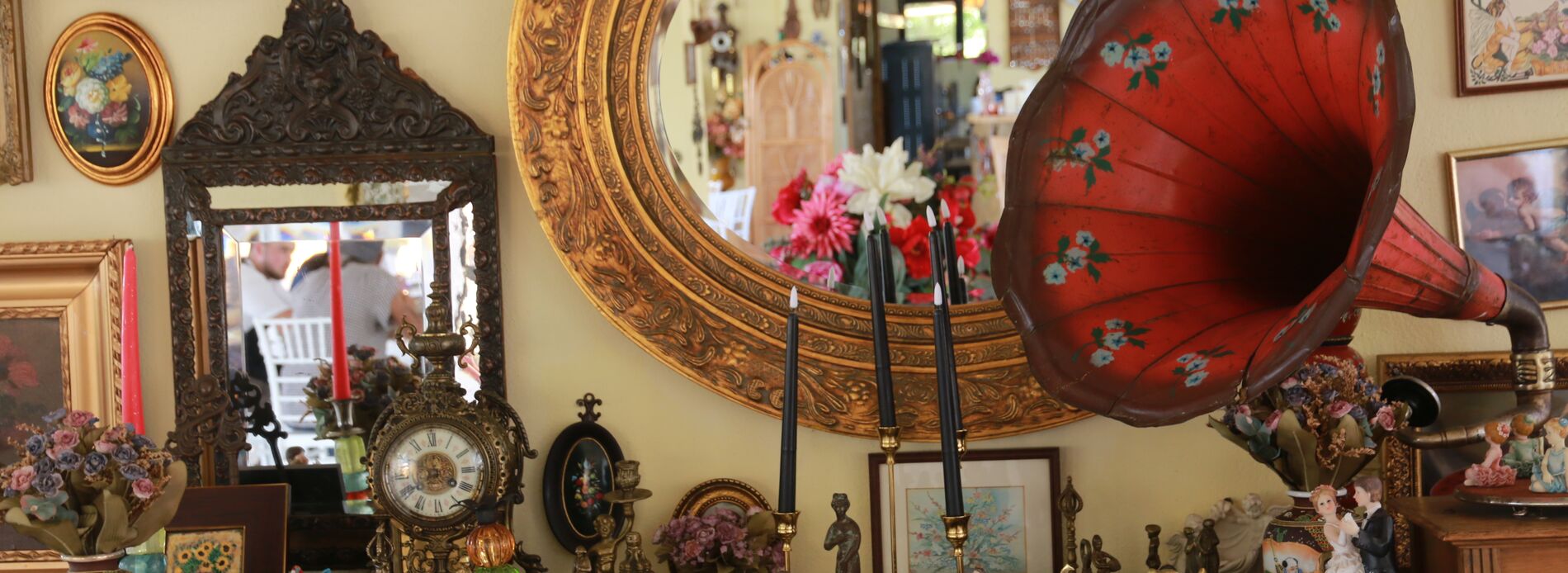 A red gramophone horn and a gilt oval mirror above the sideboard