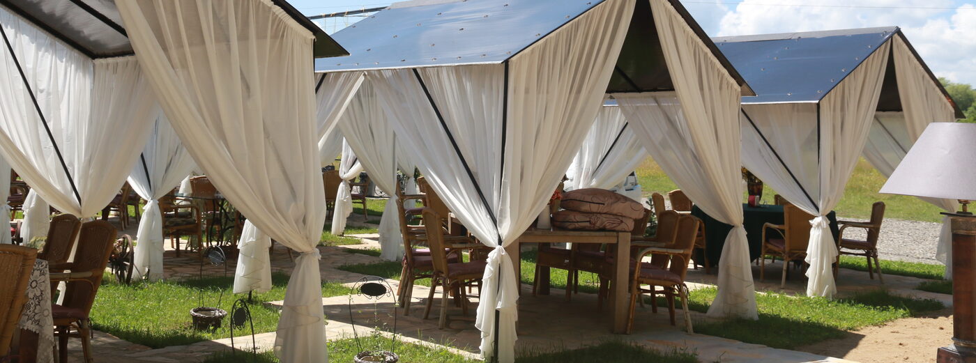 White canvas tents on the lawn, tables and wicker chairs beneath them